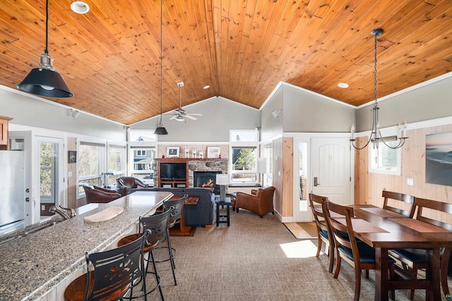 dining area with carpet, wood ceiling, a stone fireplace, ceiling fan with notable chandelier, and high vaulted ceiling