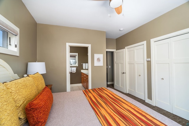 bedroom featuring a ceiling fan, baseboards, light colored carpet, two closets, and connected bathroom