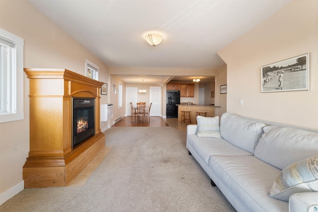 living room featuring baseboards, a glass covered fireplace, an inviting chandelier, and light carpet