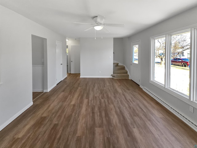 spare room featuring a baseboard heating unit, stairs, dark wood-style flooring, baseboards, and ceiling fan
