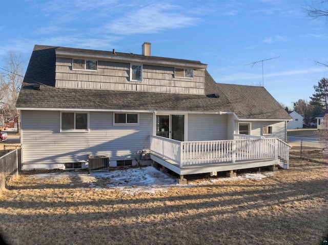 rear view of house with cooling unit, roof with shingles, fence, a wooden deck, and a chimney