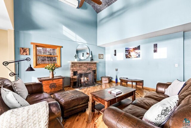 living room featuring baseboards, a brick fireplace, ceiling fan, a towering ceiling, and wood finished floors