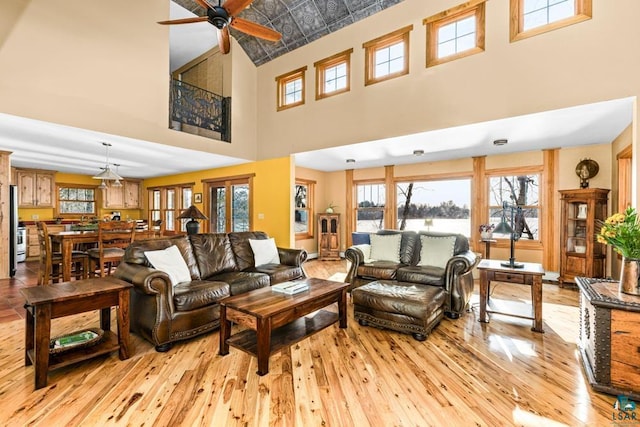 living area featuring light wood-style flooring, a ceiling fan, a high ceiling, and baseboards