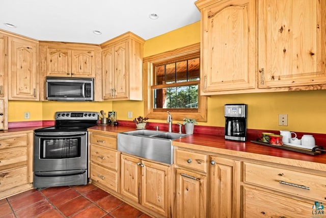 kitchen featuring a sink, dark tile patterned floors, light brown cabinetry, and stainless steel appliances
