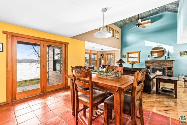 dining space featuring ceiling fan, lofted ceiling, tile patterned flooring, and a brick fireplace