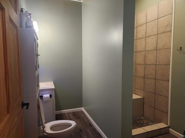 full bath with baseboards, wood finished floors, a tile shower, and toilet