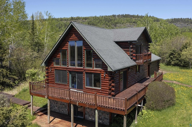 rear view of property with stone siding, a view of trees, a deck, and log siding