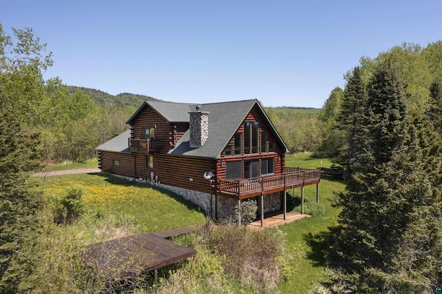view of side of property featuring a wooded view, a chimney, a lawn, a deck, and log siding
