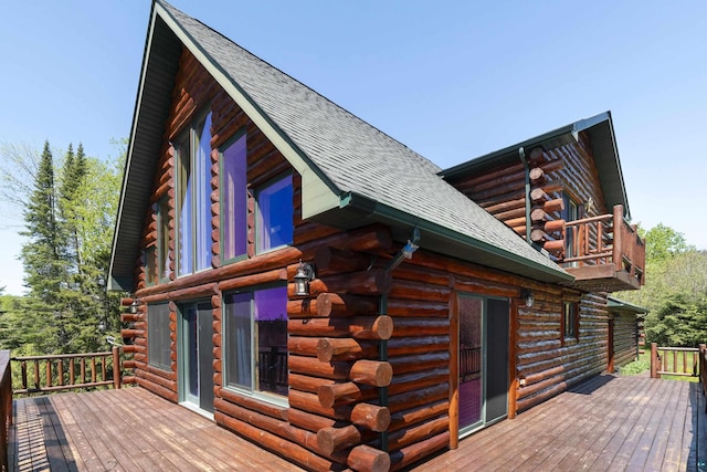 view of side of property featuring log siding, roof with shingles, a balcony, and a deck