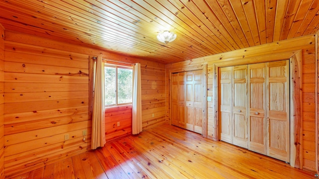 unfurnished bedroom with wood walls, light wood-style flooring, wooden ceiling, and two closets