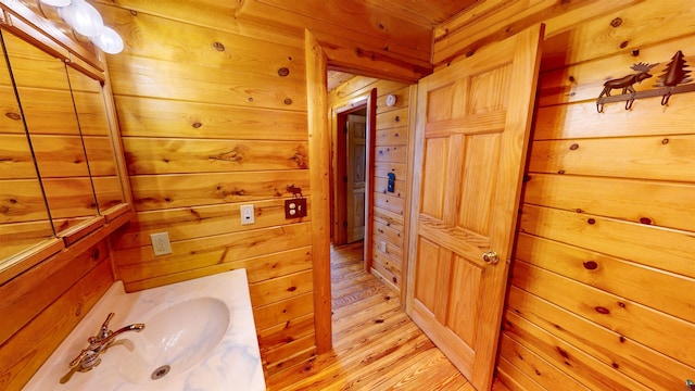 bathroom featuring wood finished floors, wooden walls, and a sink