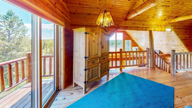 additional living space with light wood finished floors, wooden walls, an inviting chandelier, and a healthy amount of sunlight