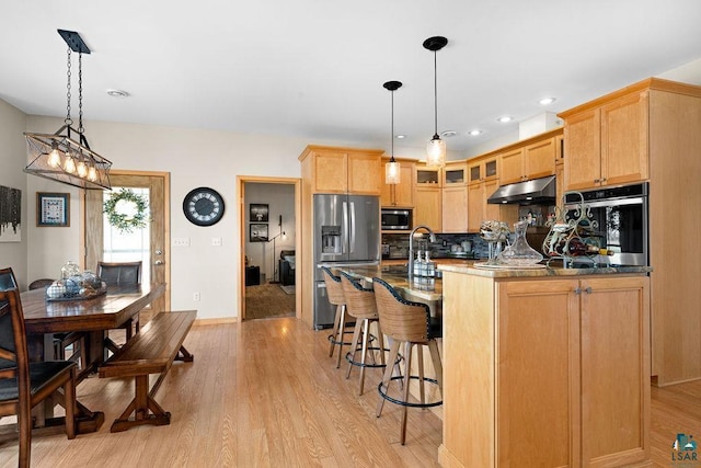 kitchen with stainless steel appliances, tasteful backsplash, a kitchen bar, light wood-style floors, and under cabinet range hood