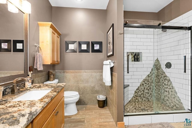 bathroom with a shower stall, toilet, vanity, and wood finished floors