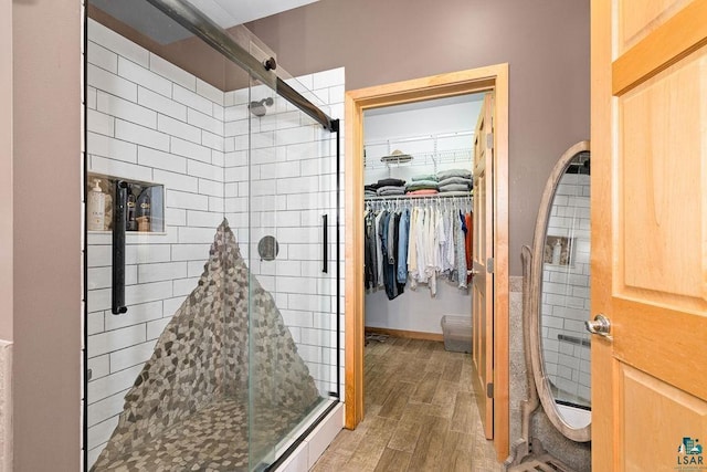 full bath with a shower stall, baseboards, a walk in closet, and wood finished floors
