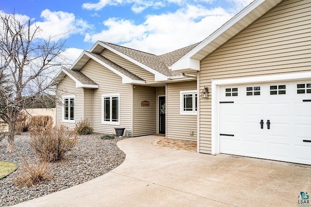 exterior space featuring concrete driveway, an attached garage, and a shingled roof
