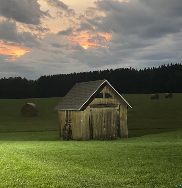 outdoor structure at dusk with a storage unit, an outdoor structure, a yard, and a wooded view