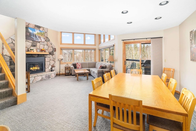 carpeted dining area with a stone fireplace, recessed lighting, and stairs