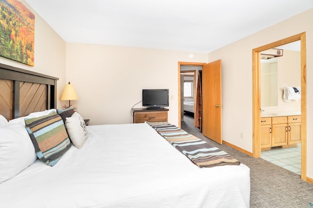 bedroom featuring baseboards, ensuite bath, light colored carpet, and a sink