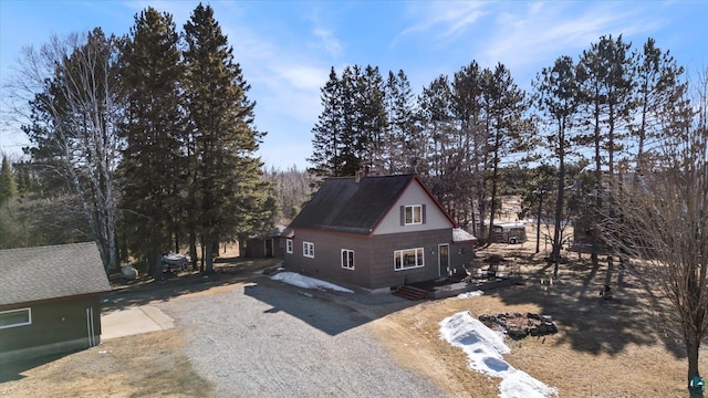 view of property exterior featuring a chimney, gravel driveway, and a shingled roof