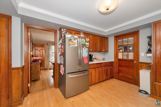 kitchen with wainscoting, brown cabinets, light wood finished floors, light countertops, and freestanding refrigerator