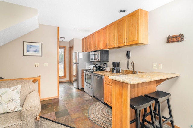 kitchen with a breakfast bar, stainless steel appliances, stone finish flooring, baseboards, and light stone countertops