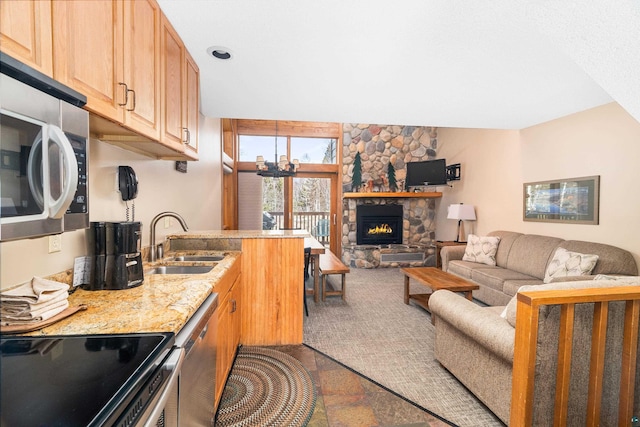 kitchen with a sink, open floor plan, a fireplace, appliances with stainless steel finishes, and light stone countertops