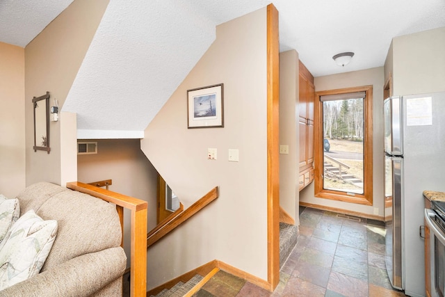 entrance foyer with stone tile flooring, a textured ceiling, baseboards, and visible vents