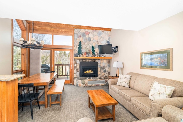 living area with a stone fireplace, carpet flooring, and a notable chandelier