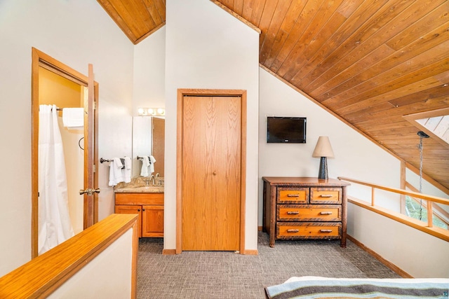 bedroom featuring ensuite bath, baseboards, light colored carpet, wooden ceiling, and lofted ceiling