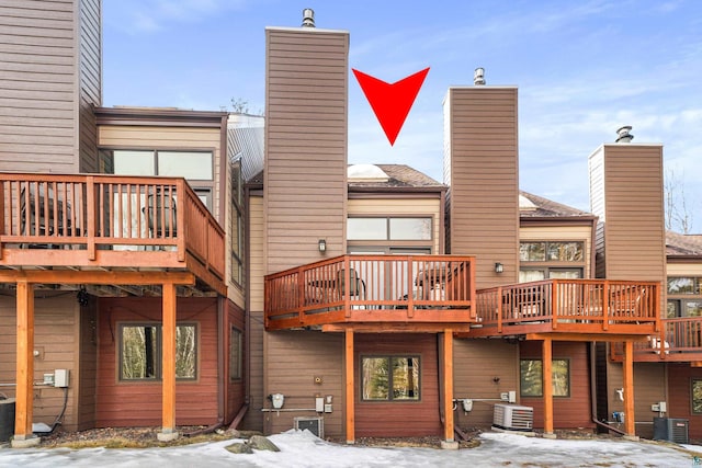 snow covered house featuring a wooden deck, central air condition unit, and a chimney