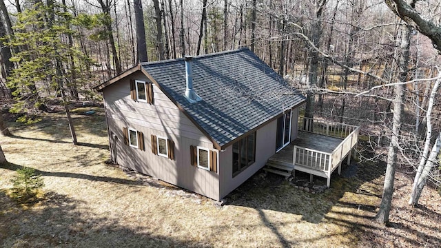 exterior space featuring a wooden deck, a shingled roof, and a view of trees