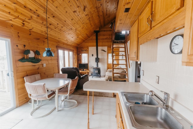 kitchen with wooden walls, vaulted ceiling, a wood stove, a sink, and open floor plan