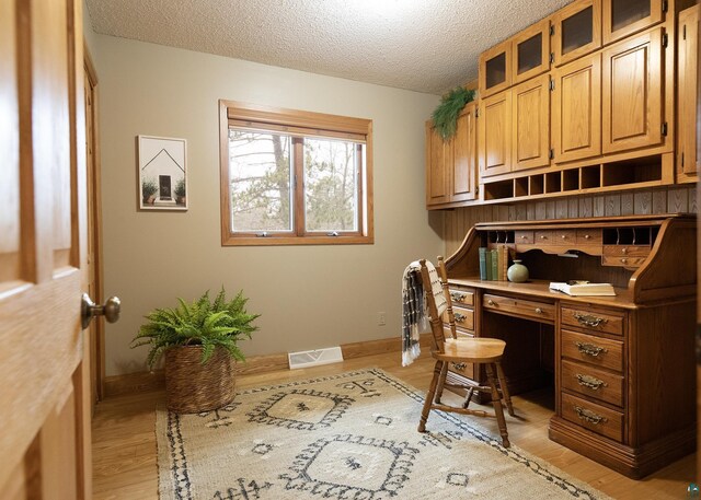 office space with baseboards, a textured ceiling, visible vents, and light wood-type flooring
