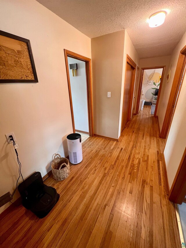 hallway featuring a textured ceiling, baseboards, and light wood-type flooring