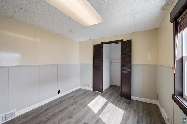 unfurnished bedroom with a wainscoted wall, visible vents, a closet, and wood finished floors