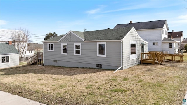 back of property featuring a deck, roof with shingles, and a lawn