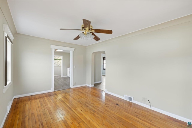 empty room with visible vents, ceiling fan, baseboards, arched walkways, and light wood-type flooring