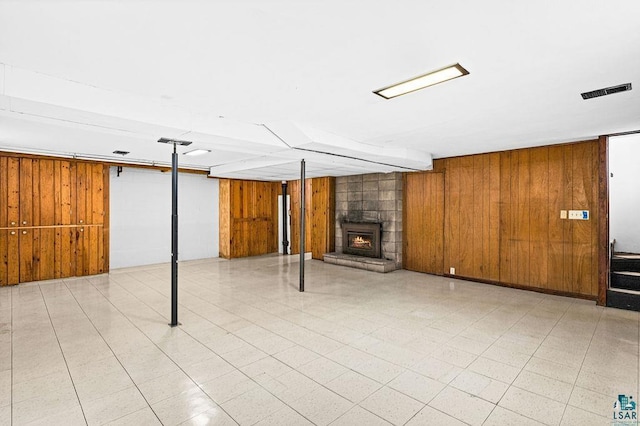 finished basement featuring wooden walls, a large fireplace, and visible vents