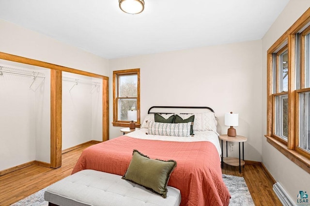 bedroom featuring a closet, baseboards, a baseboard heating unit, and wood finished floors