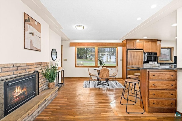 kitchen featuring oven, dark countertops, a fireplace, a kitchen bar, and hardwood / wood-style flooring