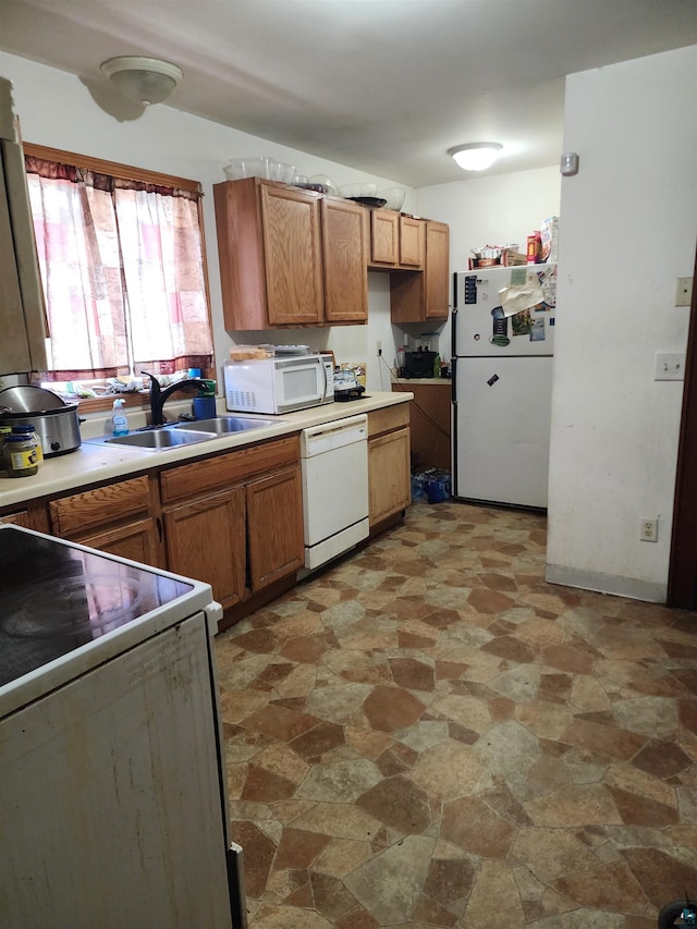 kitchen featuring a sink, stone finish flooring, light countertops, white appliances, and brown cabinetry