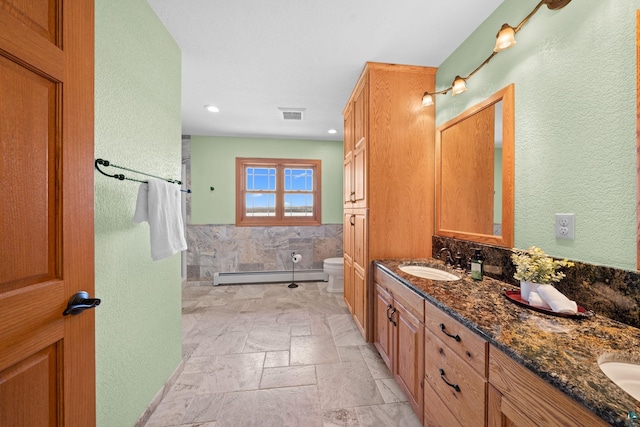 bathroom featuring a baseboard heating unit, a sink, toilet, double vanity, and visible vents