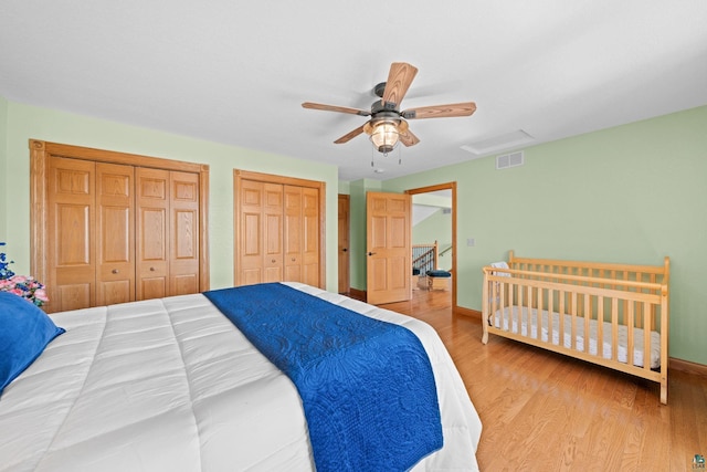 bedroom featuring multiple closets, a ceiling fan, visible vents, baseboards, and wood finished floors