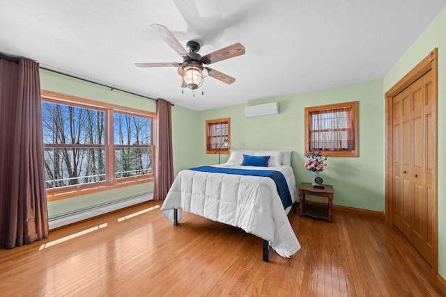 bedroom with a wall unit AC, a closet, baseboards, baseboard heating, and wood finished floors