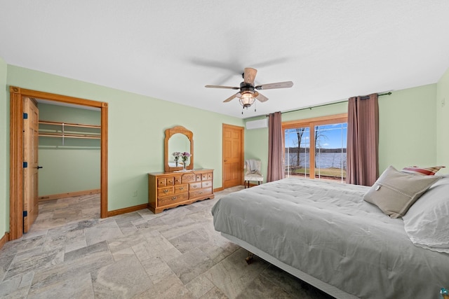 bedroom with ceiling fan, a water view, stone finish floor, baseboards, and a spacious closet