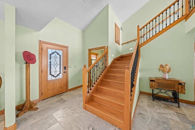entryway with baseboards, high vaulted ceiling, stone finish floor, and stairway