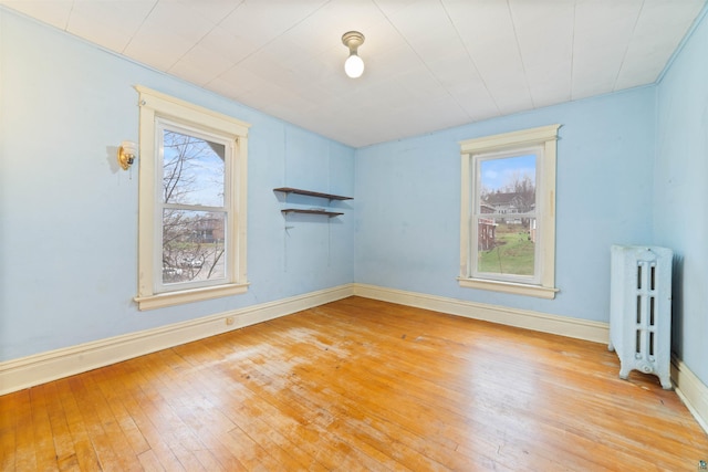unfurnished room featuring radiator heating unit, baseboards, and light wood-type flooring