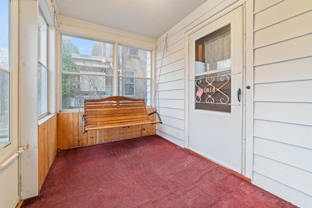 unfurnished sunroom with carpet flooring and wood walls