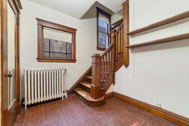 stairs with radiator heating unit, baseboards, and brick patterned floor